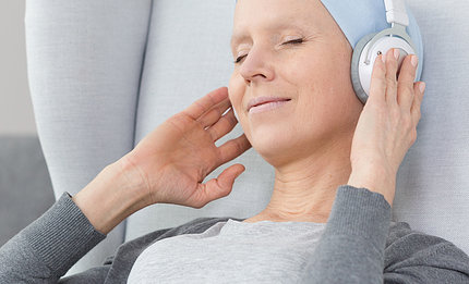 A woman wearing a beanie, eyes closed with slight smile, holds her hands up to headphones