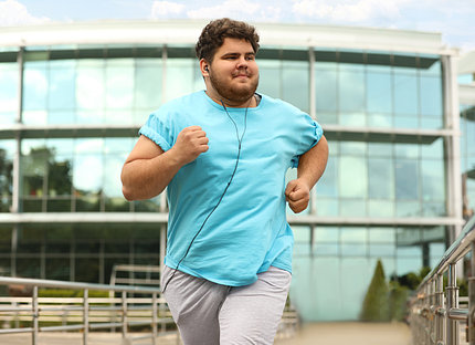 An overweight man in blue shirt jogs near office building.
