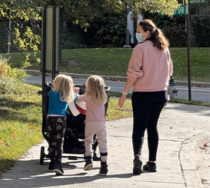 Jessica and her twin daughters who are pushing a stroller walk together on the NIH campus.
