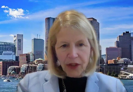 Dr. JoAnn Manson speaks on video, sitting in front of a city skyline