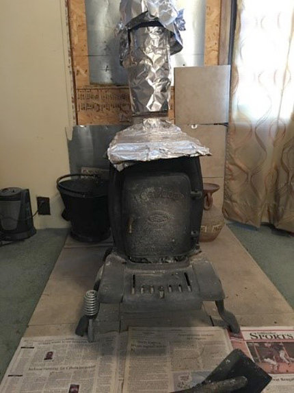 wood stove shown indoors with foil-covered pipe
