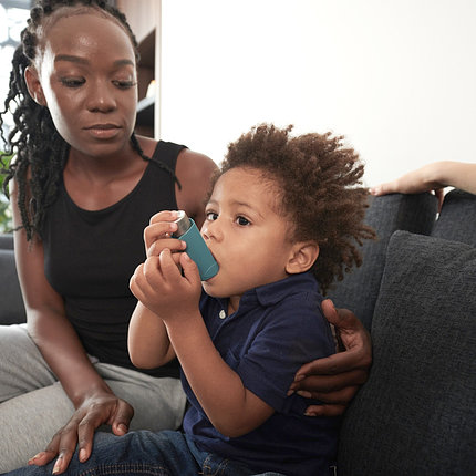African American mother with arm around young child using inhaler