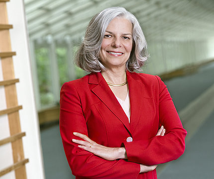 Dr. Julie Louise Gerberding stands smiling in red blazer with arms folded