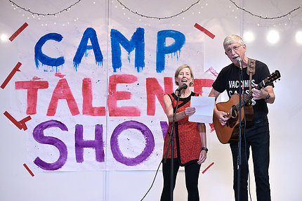With Camp Talent Show banner in background, Baker and Collins sing at mics.