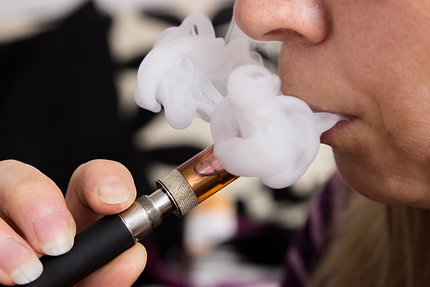 profile of woman, her hand holding an e-cigarette to her mouth, blowing out vapors