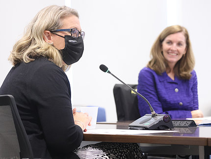 McCormick-Ell, in black mask, speaks into mic as a smiling McGowan looks on.