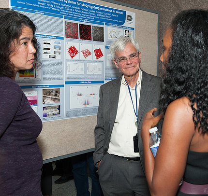 Gottesman, flanked by two female scientists, listens as a poster is explained