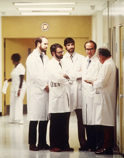 Four doctors huddle in near Nisula, all standing in white lab coats, in a Clinical Center hallway 