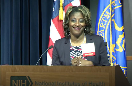 Campbell, smiling, speaks at podium.