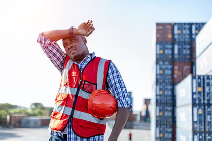 A man in a construction high vis vest wipes his brow