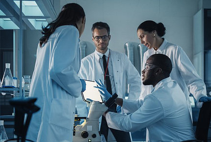 Four individuals in lab coats and gloves look at a tablet screen