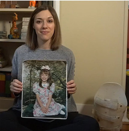 Fournier sits showing a photo of herself as a child. Next to her, a white back brace sits on the floor.