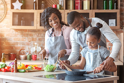 African-American woman, man, and child smile as they prepare vegetables at stove