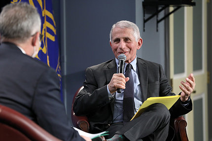 Fauci seated, holds mic