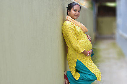 Pregnant woman stands with back to wall, cradling her baby bump.