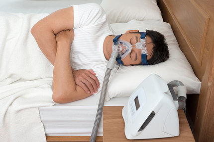 Man in white t-shirt sleeping with cpap breathing apparatus on and cpap machine in foreground