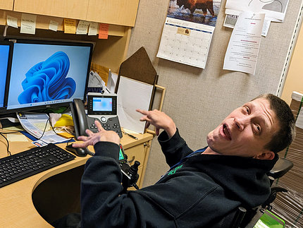 Day, wearing a black hoodie, looks up from his desk. His hands are poised over his computer keyboard.