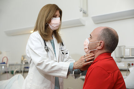 A doctor in a surgical mask conducts an exam on a patient in a surgical mask