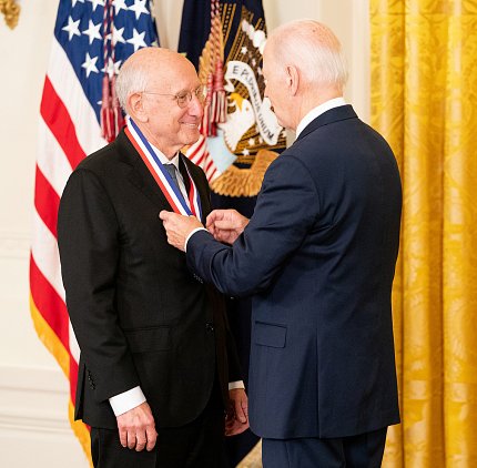 A beaming Rosenber stands while President Biden places medal around his neck.