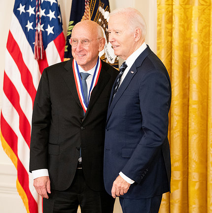 Rosenberg and Biden pose together, in front of U.S. flag, yellow curtain.