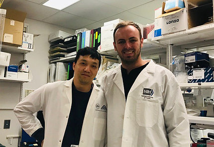 Two young researchers in white lab coats pose together in the lab.