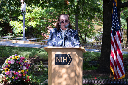 Rev. Gomez de Molina speaks at a podium, shaded by a tree
