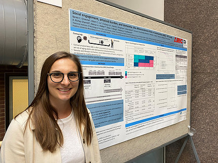 Woman wearing glasses poses with her research poster