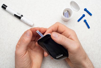 A person holds a blood glucose monitor on tiny drop of blood on their finger.