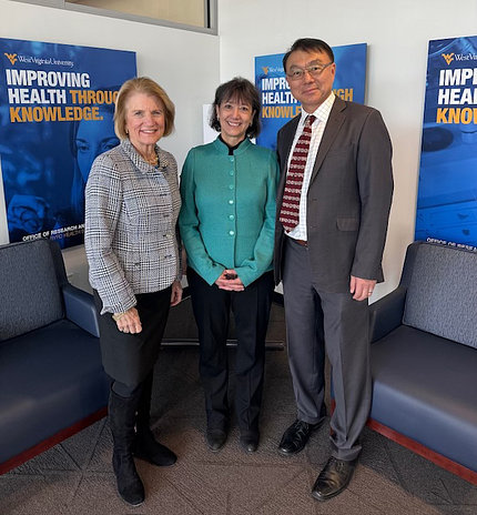 Sen. Capito, Dr. Bertagnolli and Dr. Lei pose together with blue posters behind