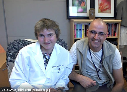 Woman in labcoat beside man wearing glasses, both smiling into camera