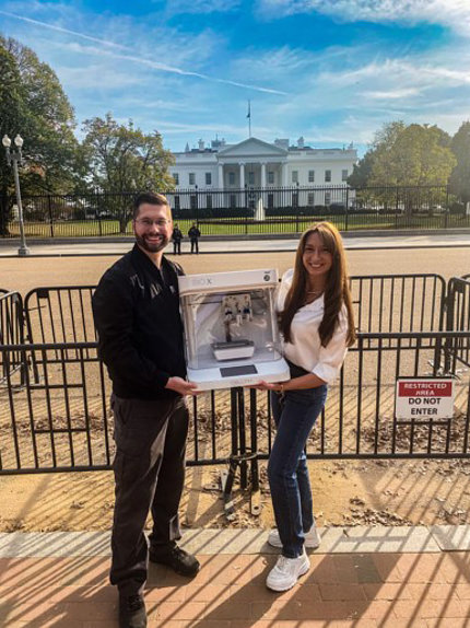 Two researchers, holding the 3-D tissue bioprinter between them, pose in front of the White House.