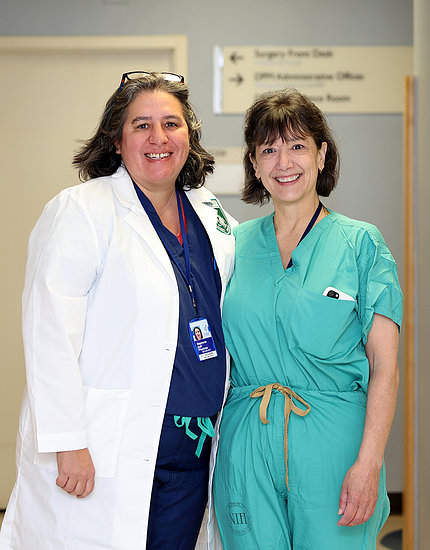 Two women smile, dressed in surgical scrubs