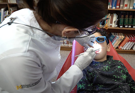 A female dentist in white lab coat looks into a child's mouth in the clinic.