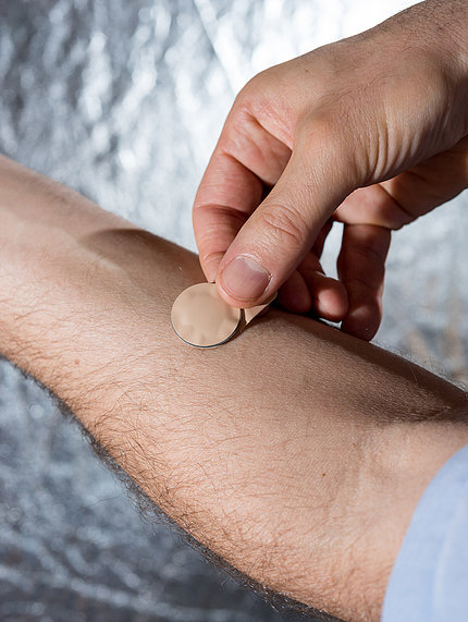 A man holds the small, round patch between his fingers as he applies it to his forearm.