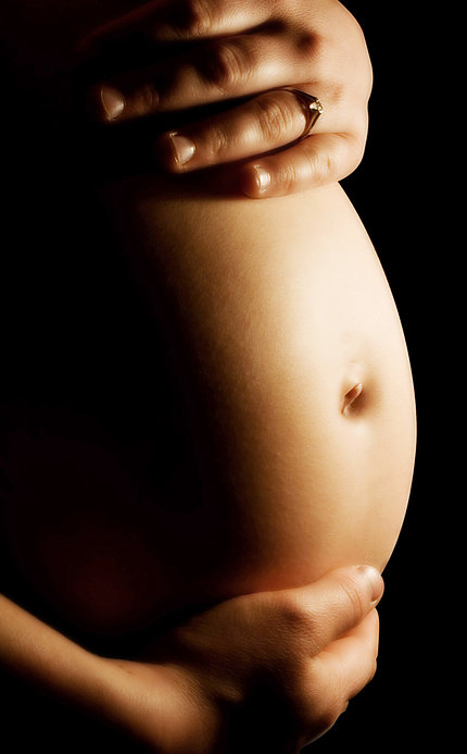 A woman's hands rest on her pregnant belly.