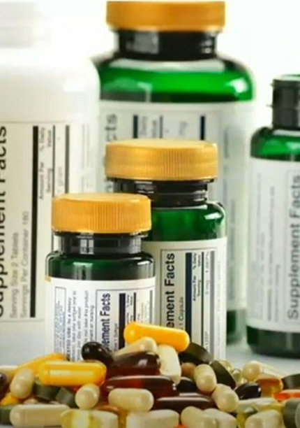 A colorful assortment of capsules sit on a table next to bottles, showing the labels of ingredients.