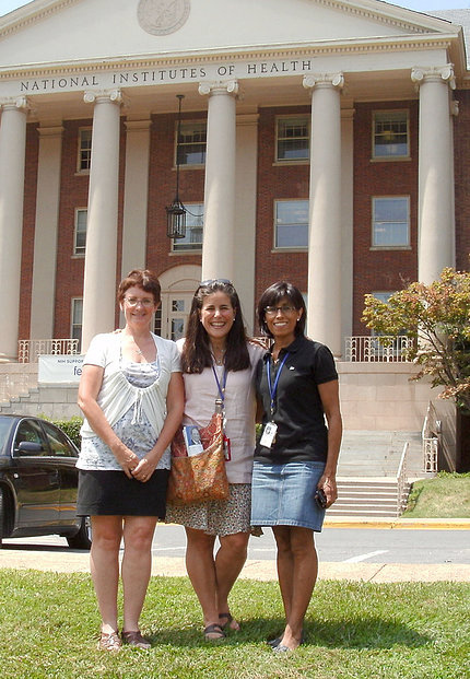 Three women smile for camera on lawn of NIH's Bldg. 1.