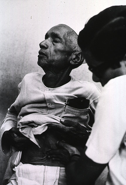 A black & white photo of an older African American man getting examined by a nurse.