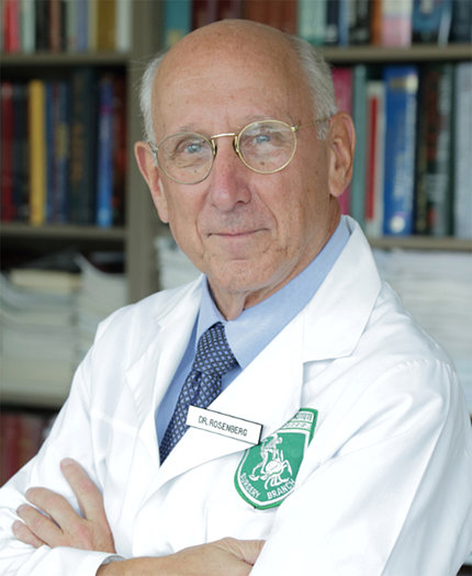Head shot of Dr. Steven Rosenberg, in white lab coat, by bookshelf