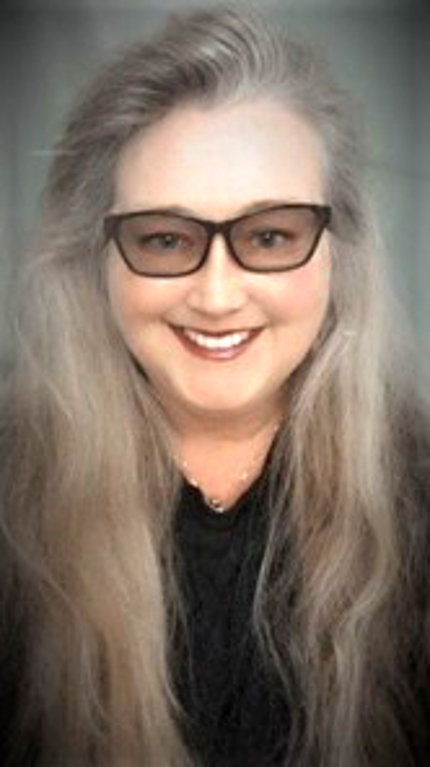 Guidone poses against a gray background. Her hair is long and light and she wears tinted glasses.
