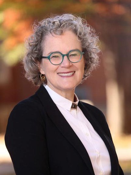 Marrazzo smiles at the camera. She has short, curly gray hair and teal glasses.