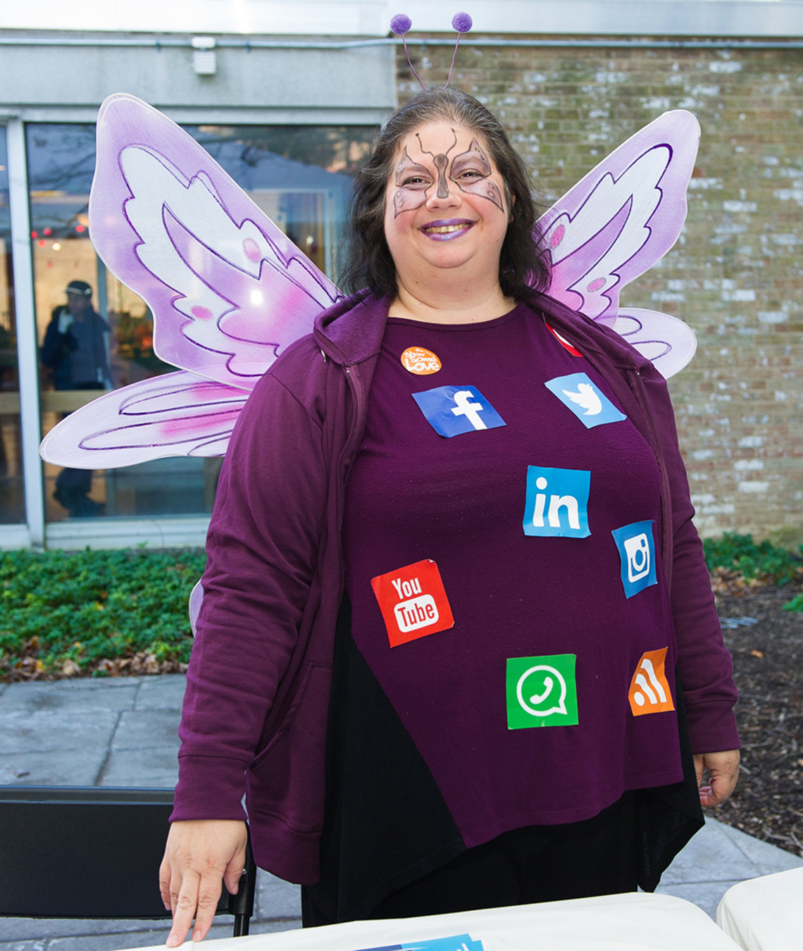 A smiling NIH'er wears social media icon stickers on purple shirt and butterfly wings