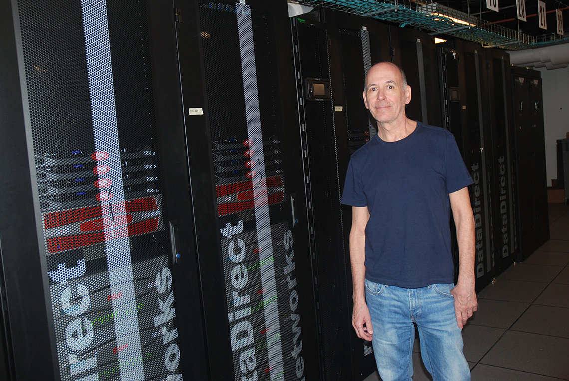 CIT's Dr. Fellini stands beside several of the many towers of the Biowulf cluster; which fill a large room in Bldg. 12.