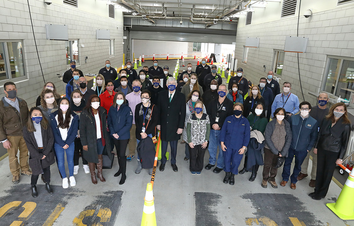 Large group of people in masks gathers for a photo with testing facility behind them