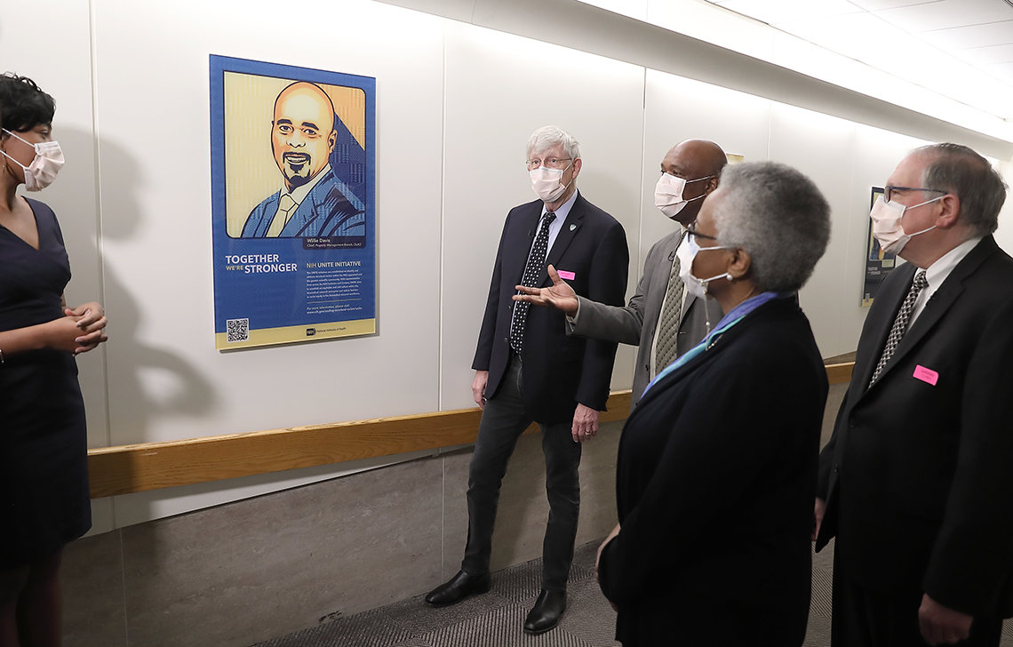 Several individuals stand in a hallway looking at a newly hung portrait