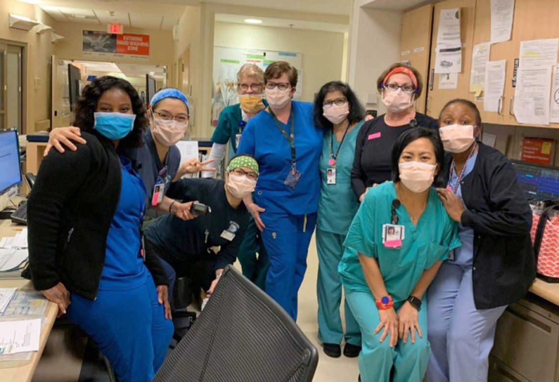 Several people dressed in scrubs and masks smile into camera.