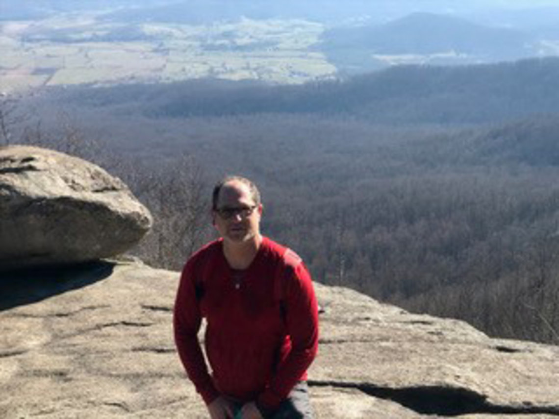 Steve Friedman, in red sweatshirt and sunglasses, stands atop Old Rag Mountain