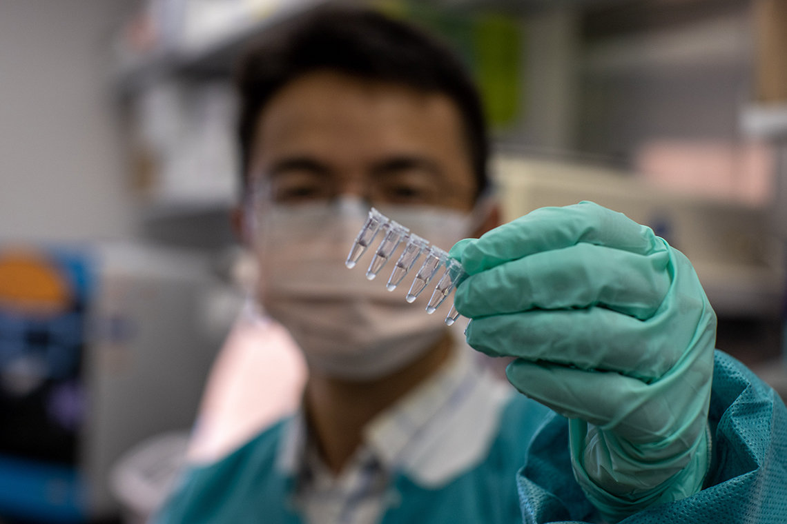 A masked and scrubbed Guan holds up test tubes 