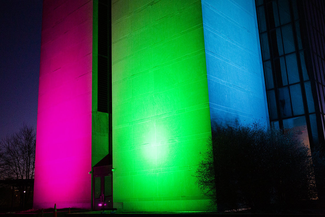 The side of a building on campus is lit up red, green and blue at night. 