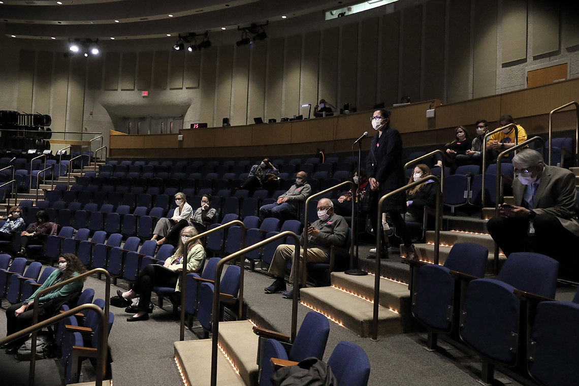 A masked member of the audience asks a question in a physically-distanced auditorium 